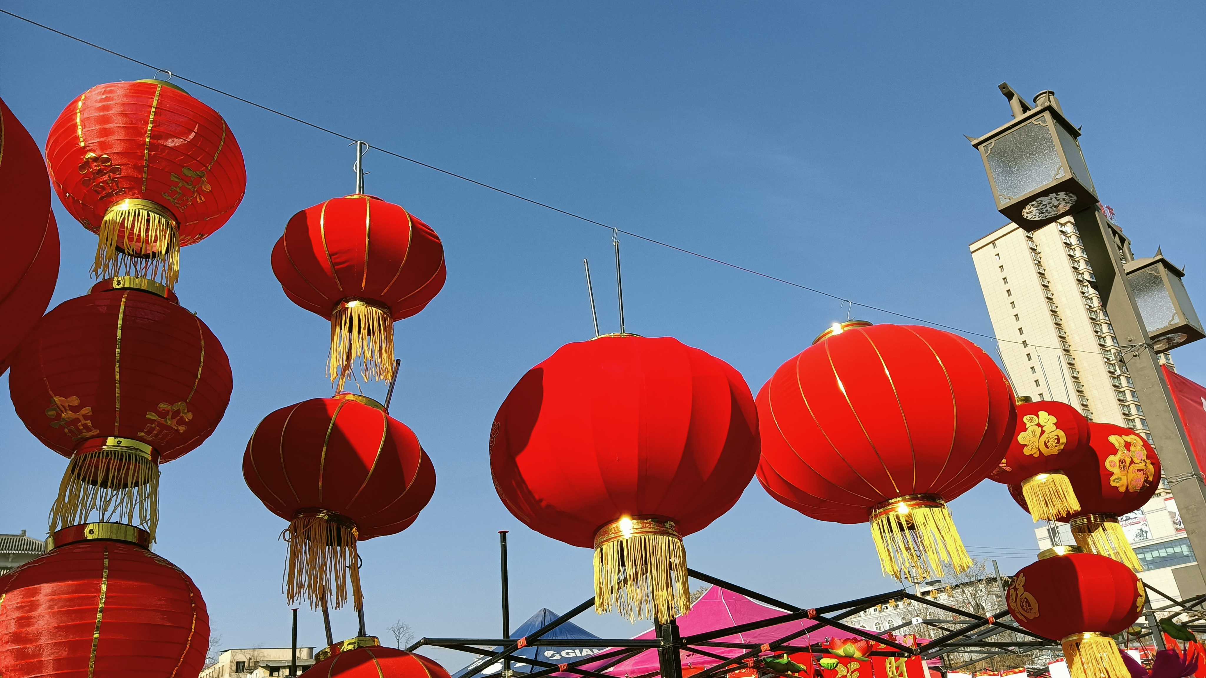 朗日晴空下，春光明媚，一串串红灯笼挂在高处，供人采办，蔚蓝的天空与火红的灯笼形成了鲜明的对比，金色的流苏作配饰，最后就再加上午后光影照射形成明暗阴影，更加具有中国风韵。
