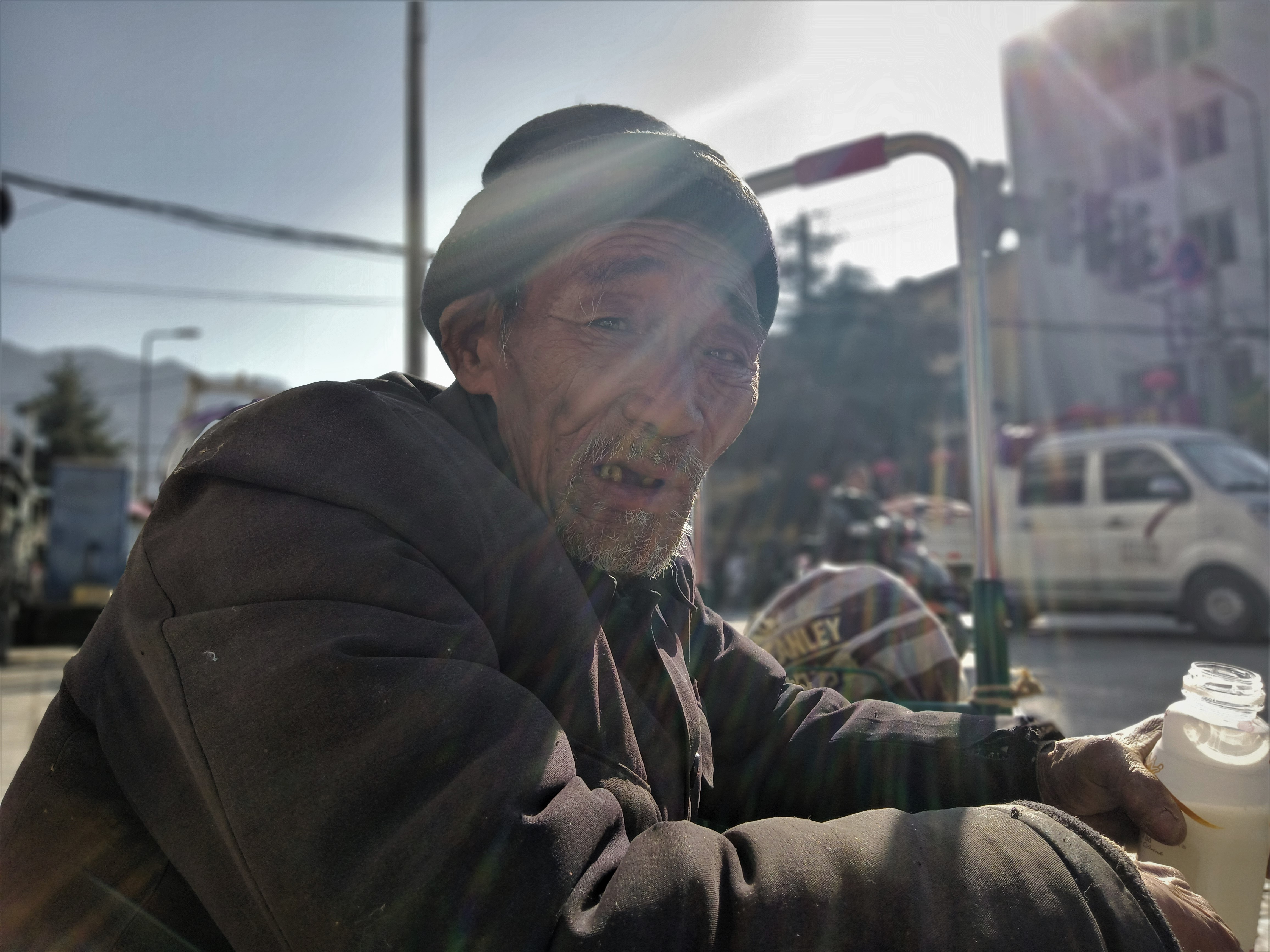 他一个人孤零零的坐在马路边上喝着一瓶酸奶。很巧的是，在相机定格的那一瞬间老爷爷那双浑浊的眼睛正好对上了镜头，那张饱经风霜的脸上写满了故事........