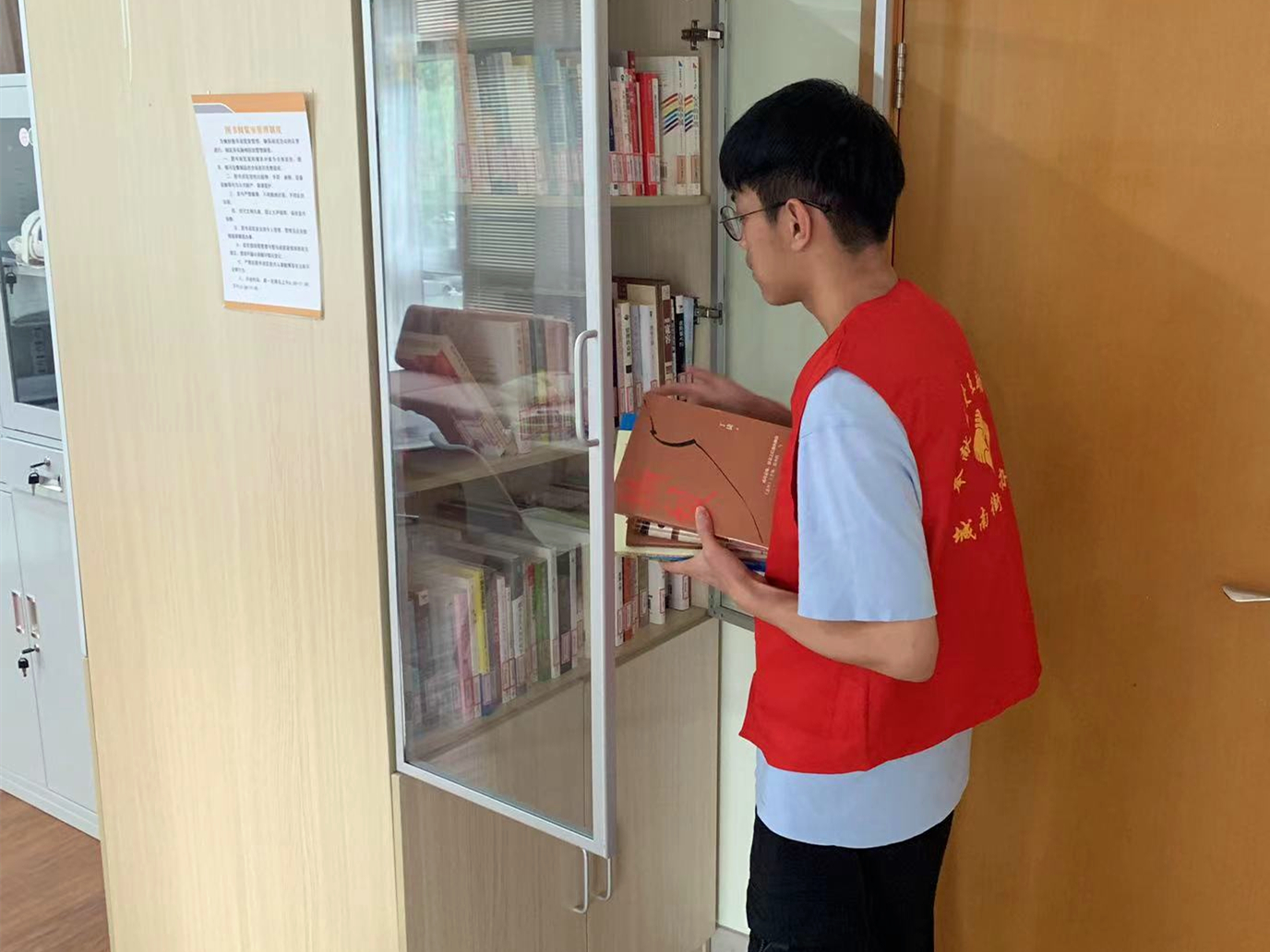 图为学生葛宇恒在江苏省苏州市张家港市城南街道参与社区新时代文明实践活动，为图书室提供卫生打扫、图书整理及借阅登记服务。